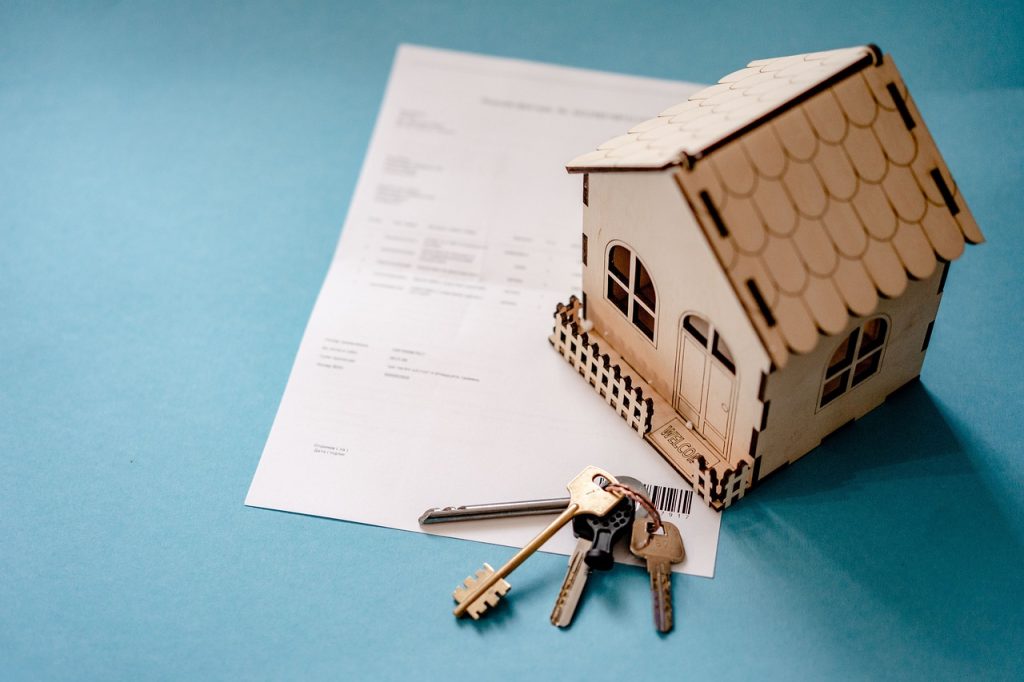 Miniature house with keys on a mortgage document, symbolising real estate and homeownership on a blue background